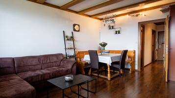 Un salon chaleureux avec un canapé en cuir marron, une petite table et un coin repas comprenant une table et des chaises en bois.