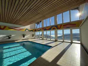Piscina interior con vistas a montañas a través de grandes ventanales.