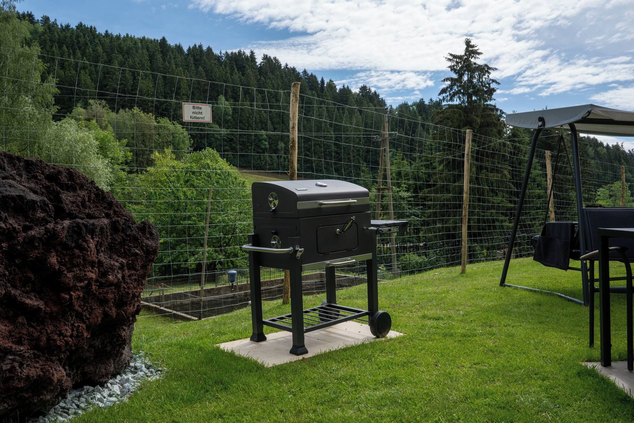En grillplats i ett inhägnat utomhusområde med utsikt över en skogbeklädd kulle.