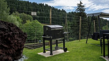 En grillplats i ett inhägnat utomhusområde med utsikt över en skogbeklädd kulle.