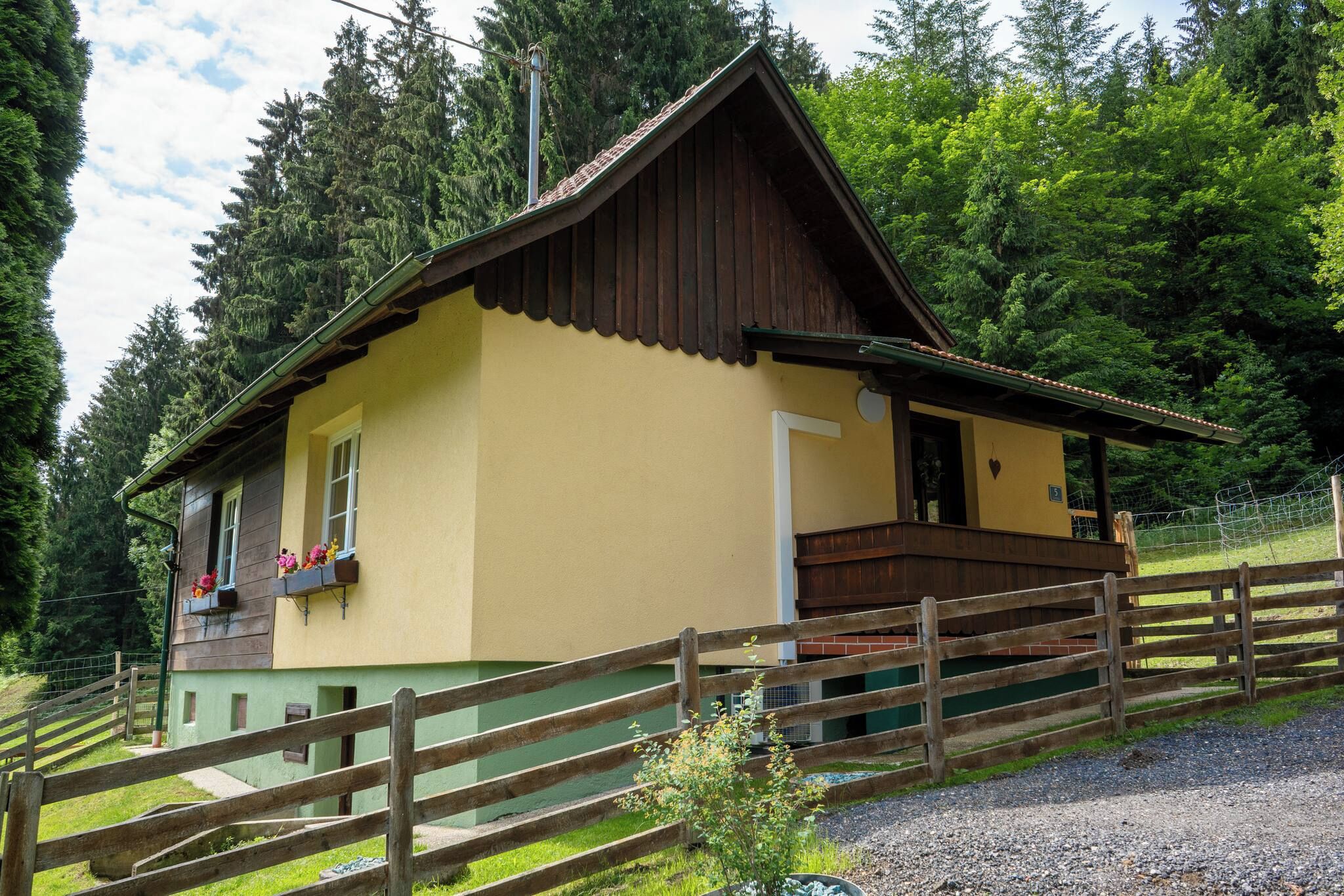 A wooden house with a balcony, surrounded by a wooden fence and greenery.