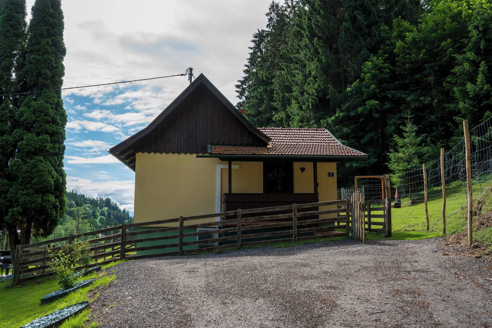 A small, single-story building with a sloped roof, a wooden fence, and a gravel driveway.