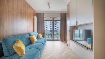 Uma sala de estar moderna com um sofá azul, televisão e vista para um prédio residencial.
