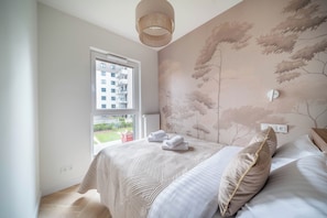 Quarto com uma janela grande, cama com almofadas e um mural de árvore na parede.