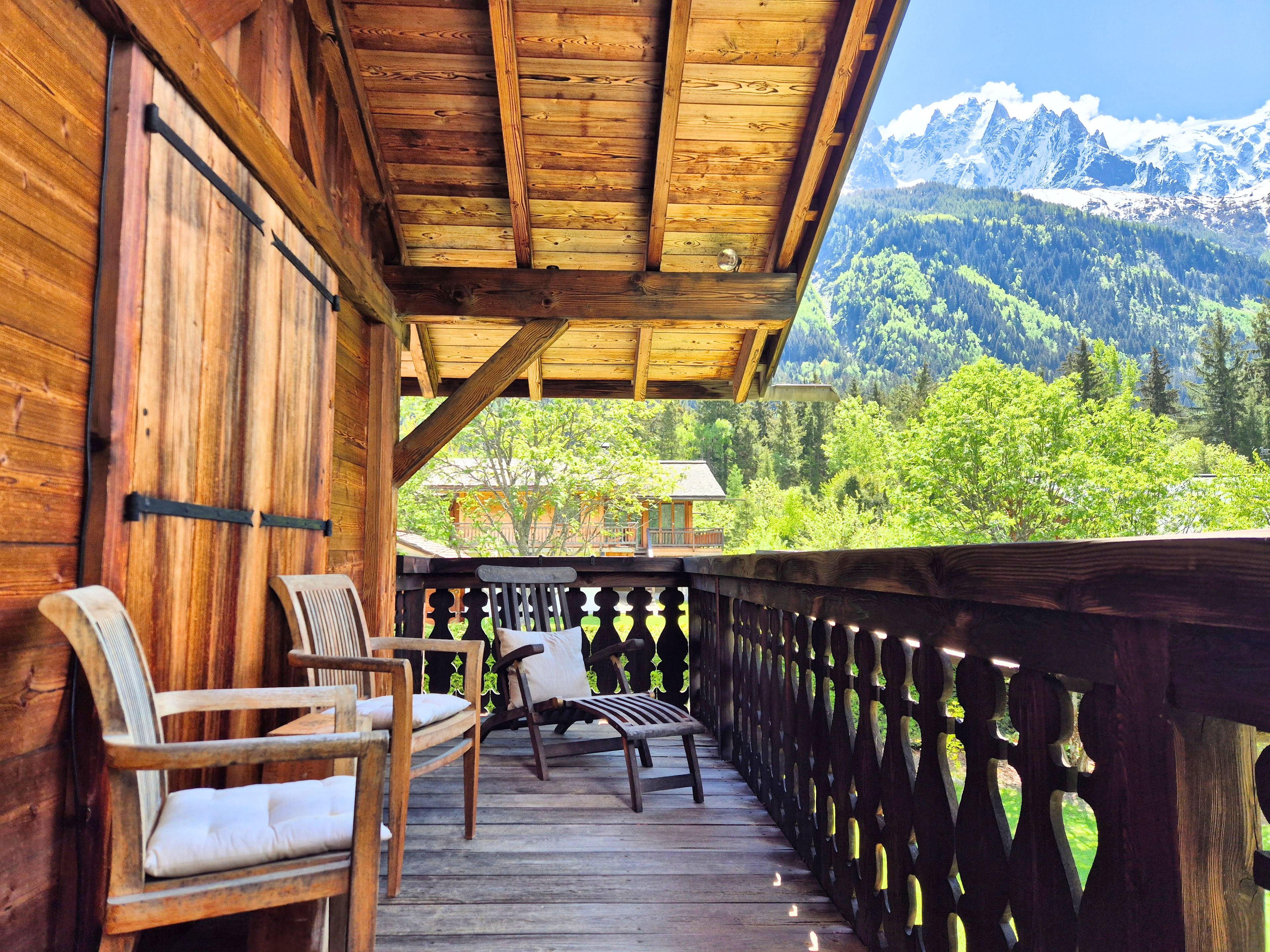 A wooden deck with two chairs and a table, overlooking a mountainous landscape.