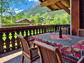 Eine Holzterrasse mit einem für zwei Personen gedecktem Tisch, mit Blick auf eine gebirgige Landschaft.