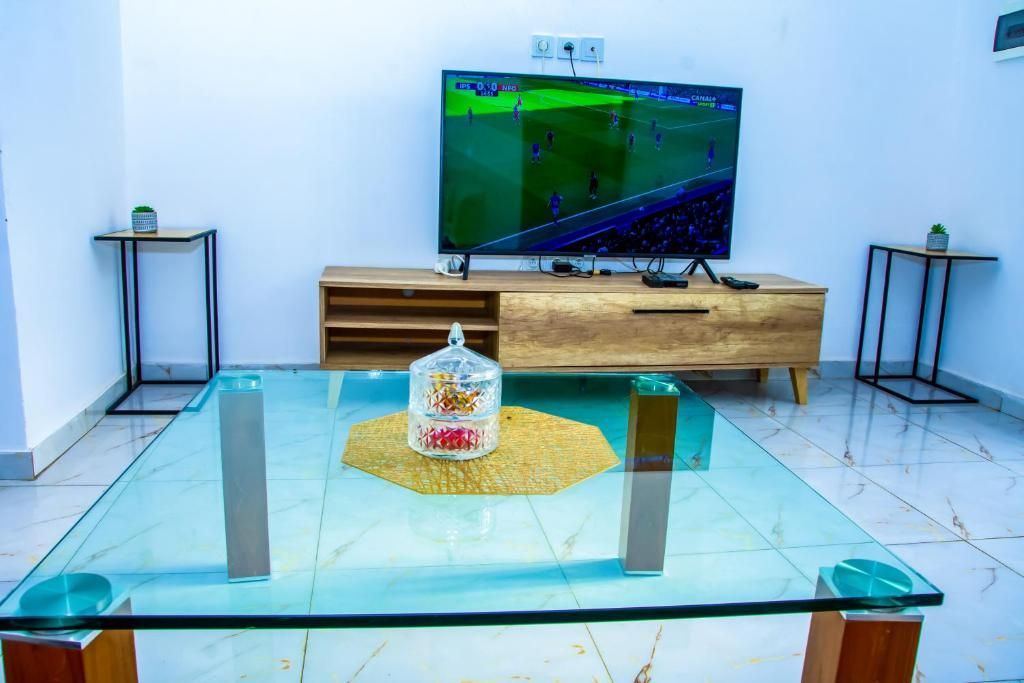 A room with a glass-top table, a wooden cabinet, and a television displaying a sports game.