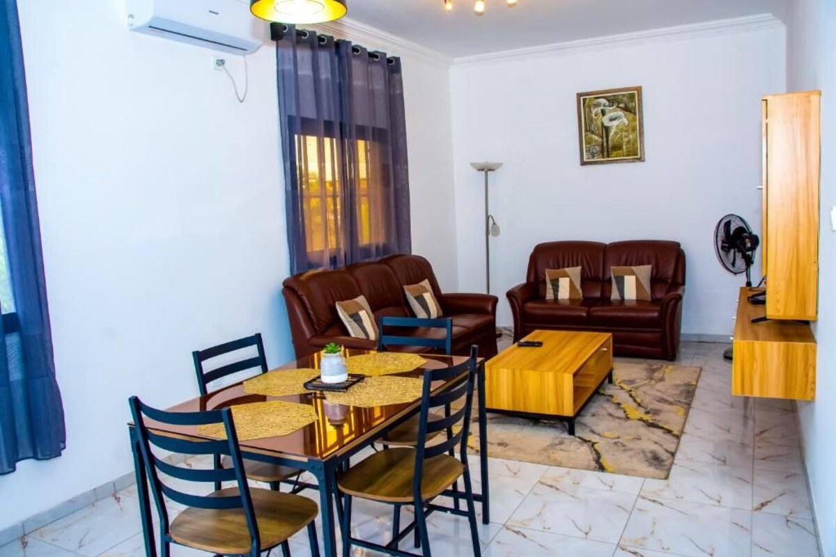 A living room with a brown leather sofa, a wooden coffee table, and a dining table with chairs.