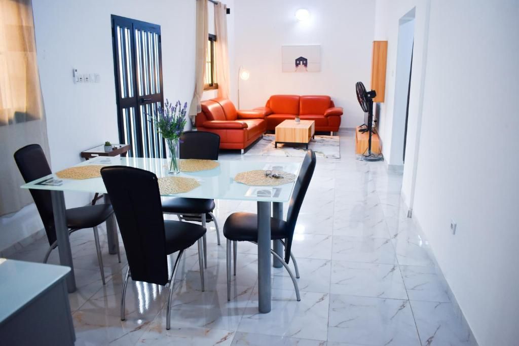 Een moderne woonkamer met een glazen eettafel, zwarte stoelen, een rode bank en een staande ventilator.