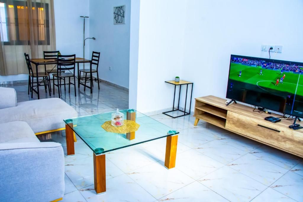 A modern living room with a glass coffee table, a sofa, a TV, and a dining area with chairs.