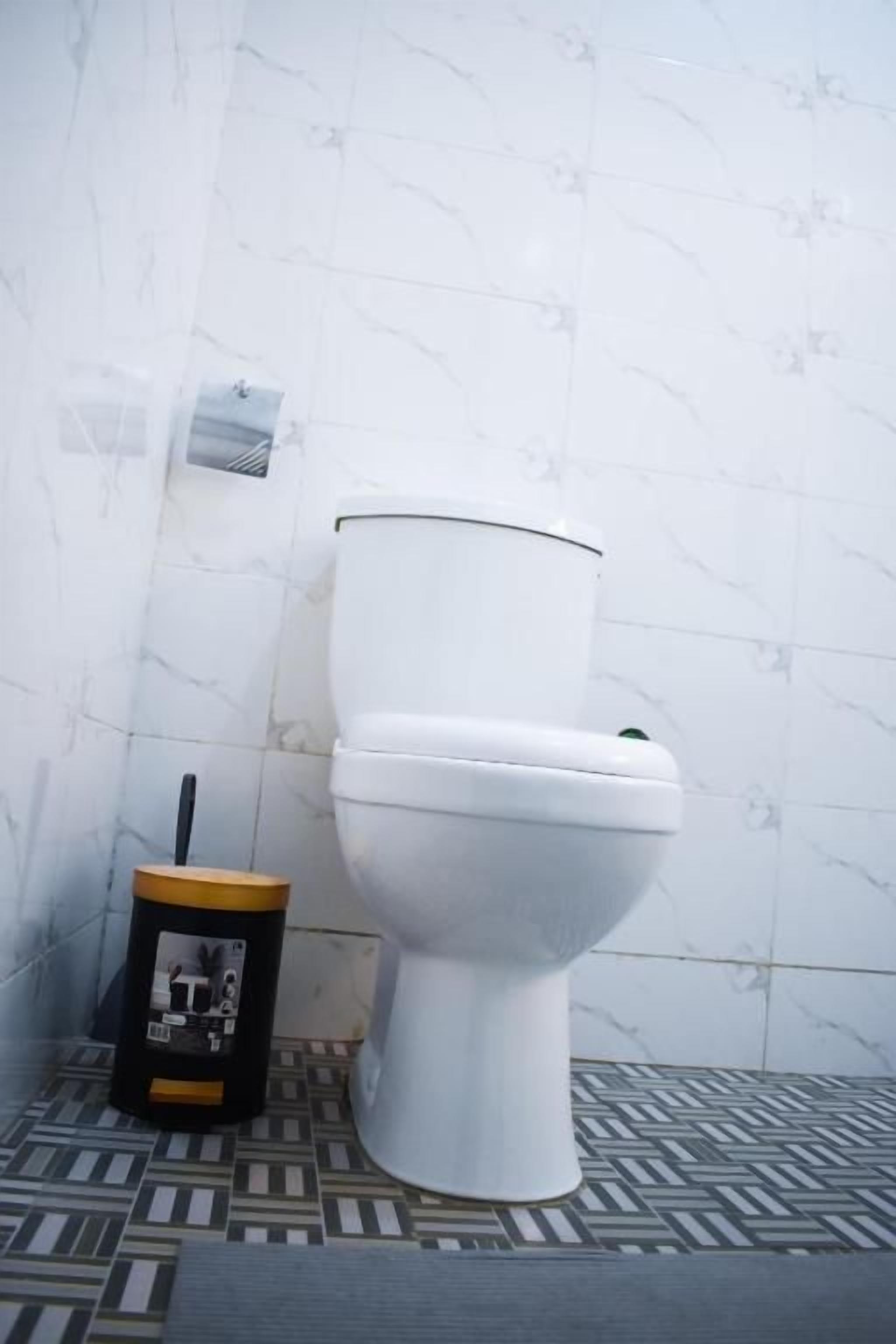 Eine Toilette mit weißem Tank und Deckel, einem schwarzen und goldenen Mülleimer und einem gemusterten Boden.