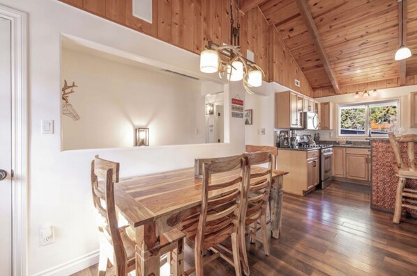 Una cocina rústica con armarios de madera, un comedor con mesa y sillas de madera, y una lámpara colgante.