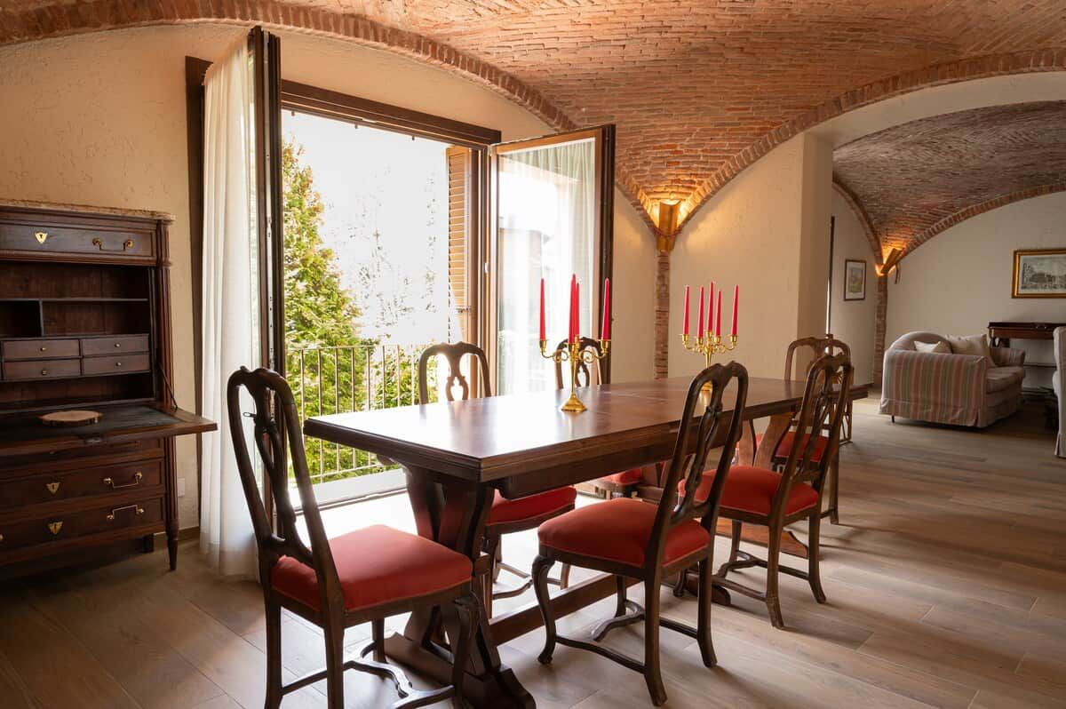 A dining area with a wooden table and chairs, a view through a glass door, and a brick ceiling.