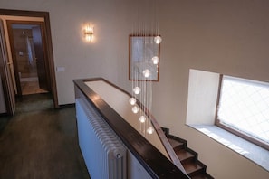 Una escala amb barana de fusta, un radiador i un lluminari fixat a la paret.