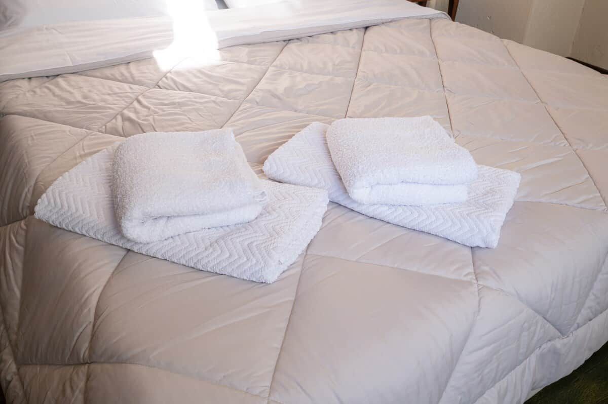Een bed met een gewatteerd wit matras en twee opgevouwen witte handdoeken.