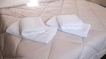 Een bed met een gewatteerd wit matras en twee opgevouwen witte handdoeken.