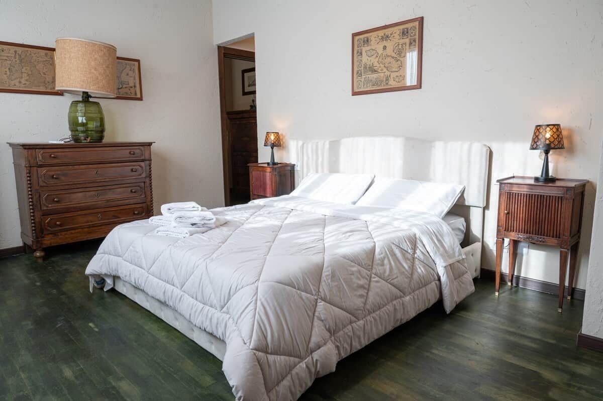 A neatly made bed with a white duvet, a wooden dresser with drawers, two bedside tables with lamps, and a framed picture on the wall.