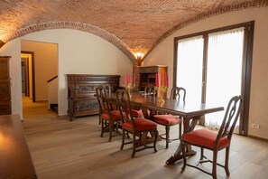 A dining area with a wooden table and chairs, a fireplace, and a view through a large window. - Rustic Home | Villa with a Garden on the Lake (Ispra)