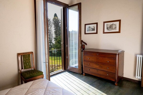 A bedroom with a bed, a wooden dresser, a chair, and a sliding glass door leading to a balcony.