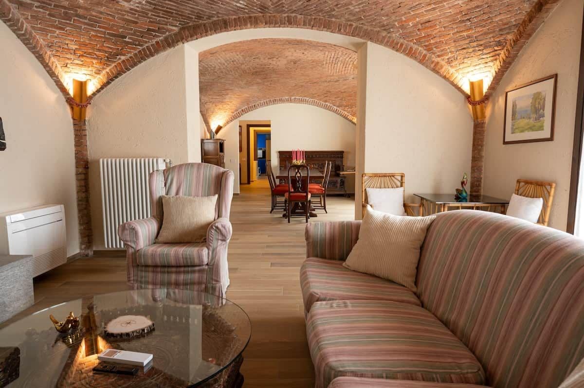 A cozy living room with a brick ceiling, striped sofas, a glass coffee table, and a fireplace.