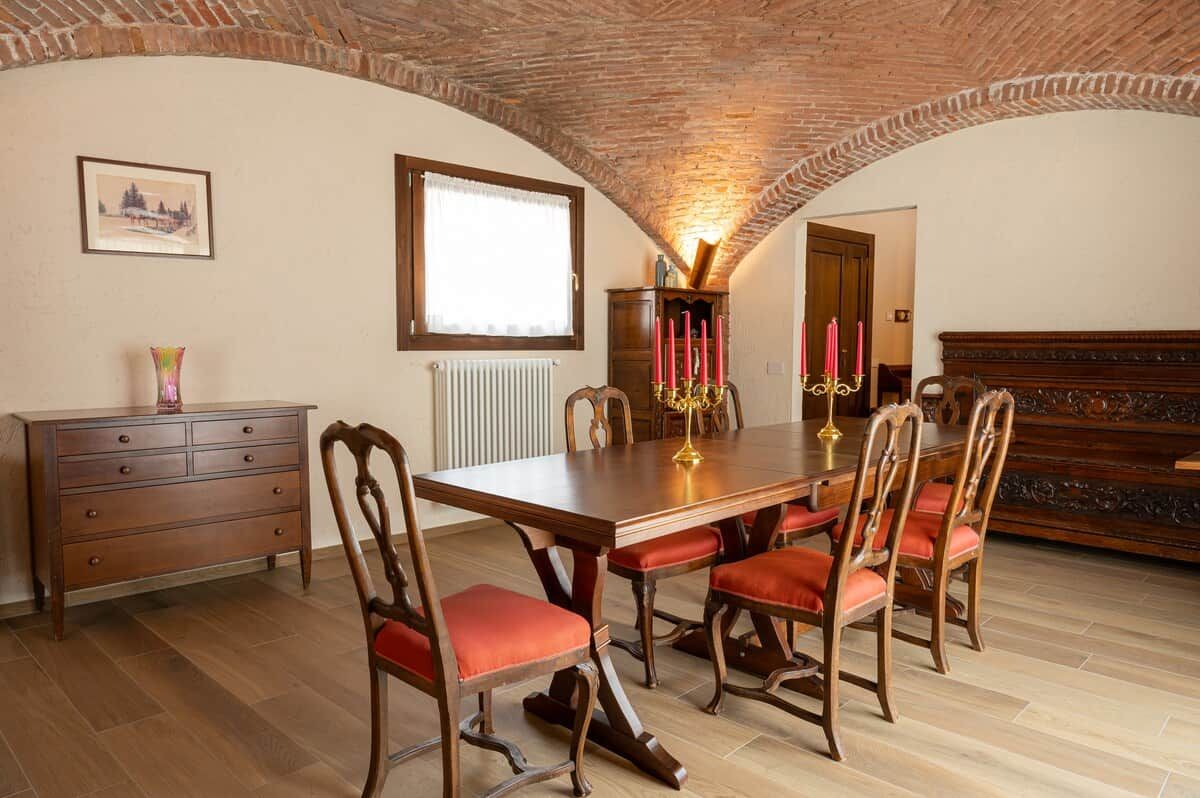 Comedor con una mesa de madera, sillas tapizadas rojas, un aparador de madera y techo de ladrillo.