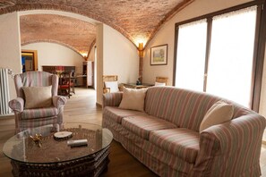 A living room with a striped sofa, armchairs, a glass coffee table, and a brick ceiling.