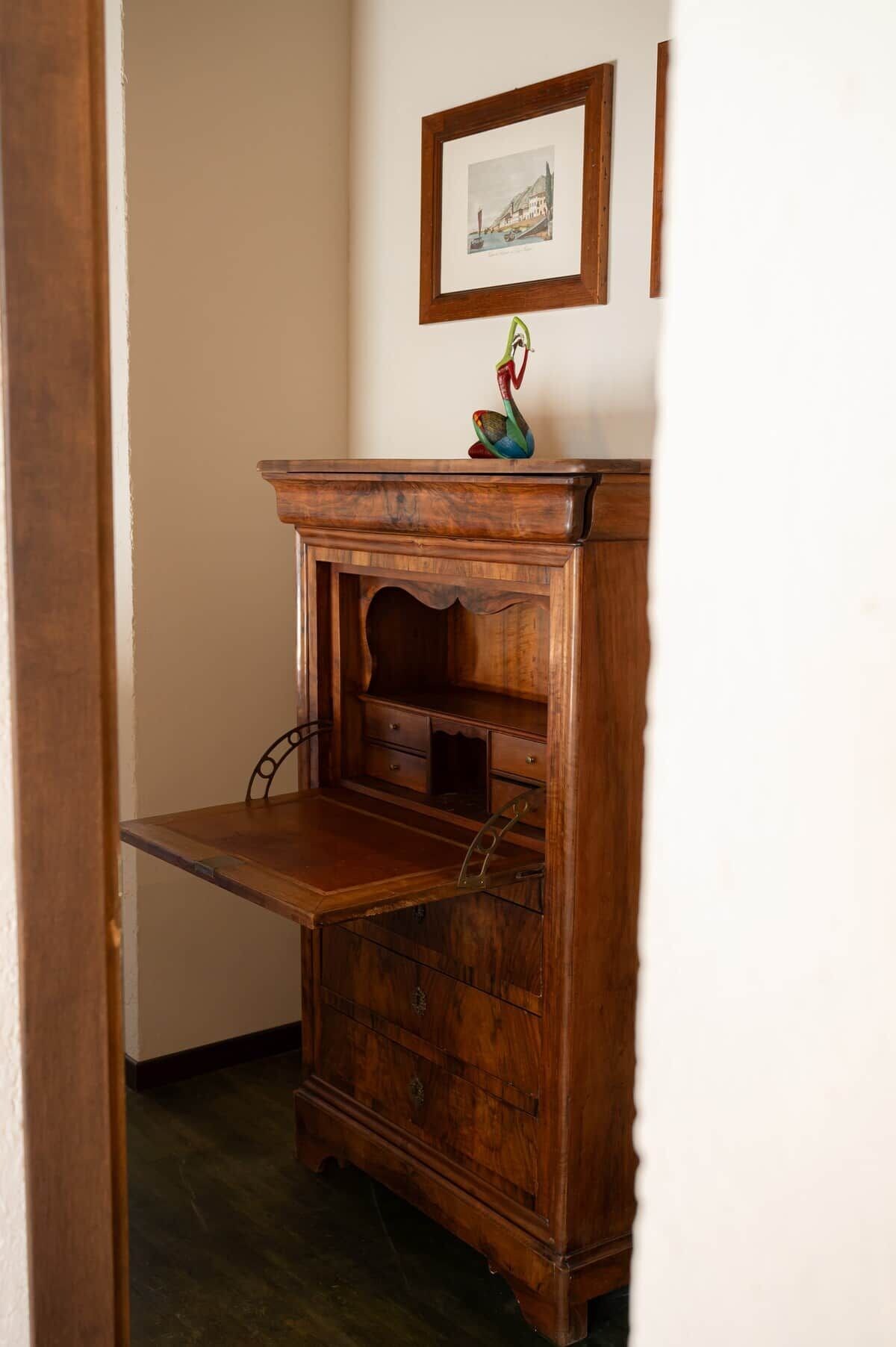 Un escritorio de madera con cajones y estante, ubicado en una habitación con pared blanca y un cuadro enmarcado encima.