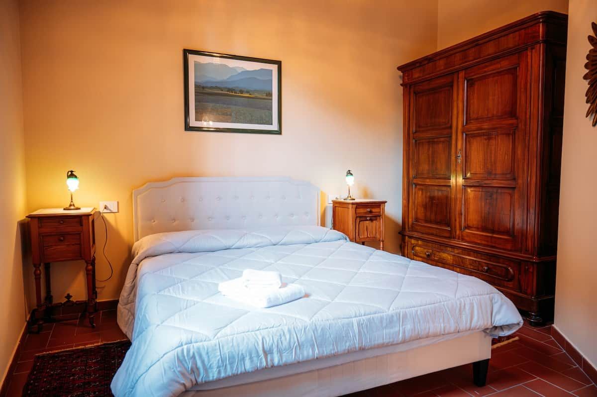 A bedroom with a bed, bedside lamps, a wooden wardrobe, and a framed picture on the wall.