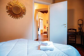 A hotel room with a bed, a door leading to a corridor, and a wall-mounted mirror. - Love's Nest | A Romantic Getaway on Lake Maggiore (Ispra)