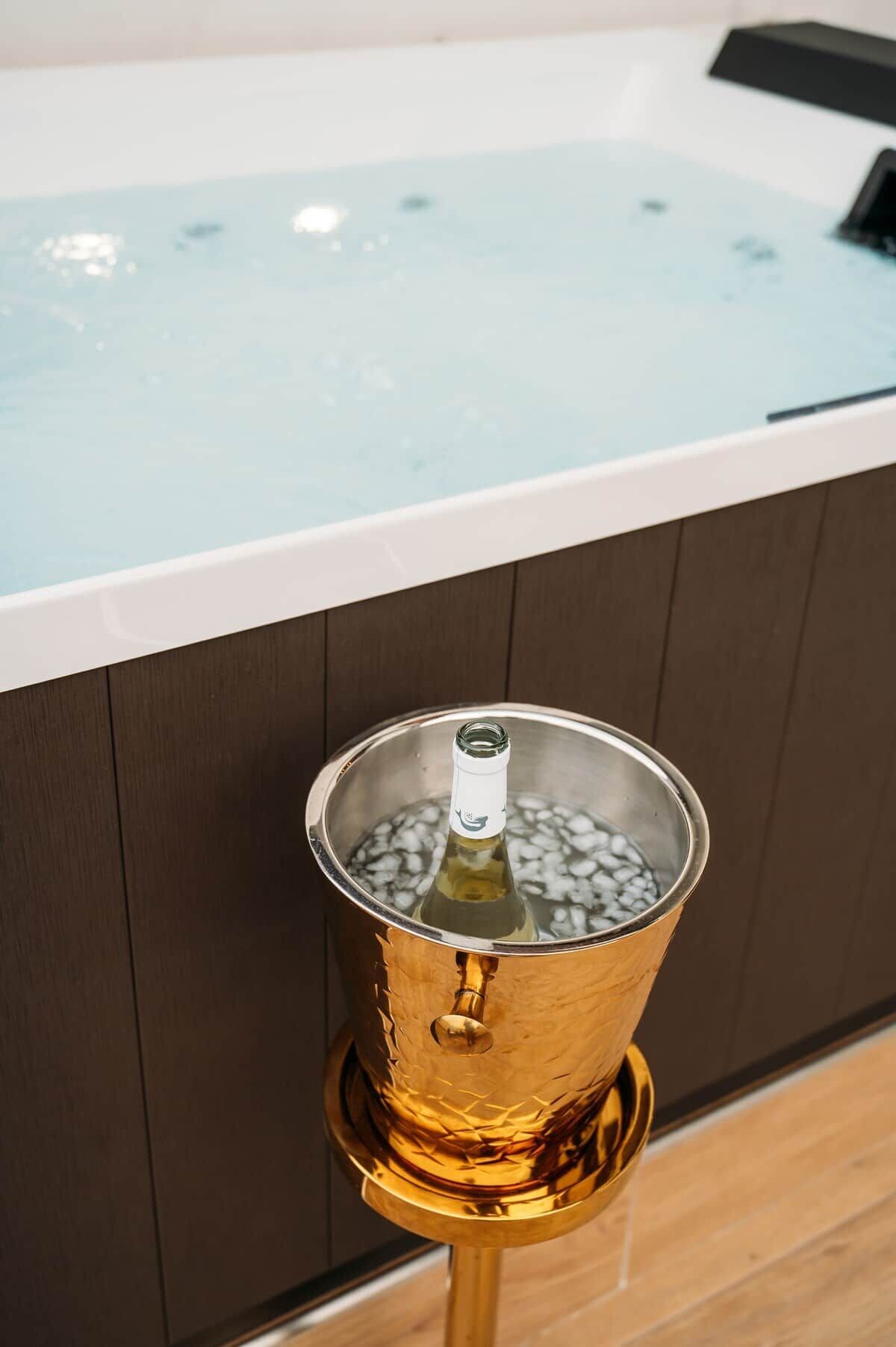 Un bain à remous avec une vue dégagée sur l’eau, une bouteille de vin dans un seau en métal et un plancher en bois.