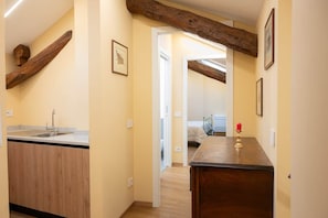 A narrow hallway with wooden beams, a kitchen area with a sink, and a bedside table with a candle.