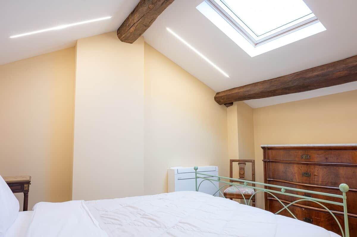 Un dormitorio con tragaluz, cama, cómoda y mesita de noche.