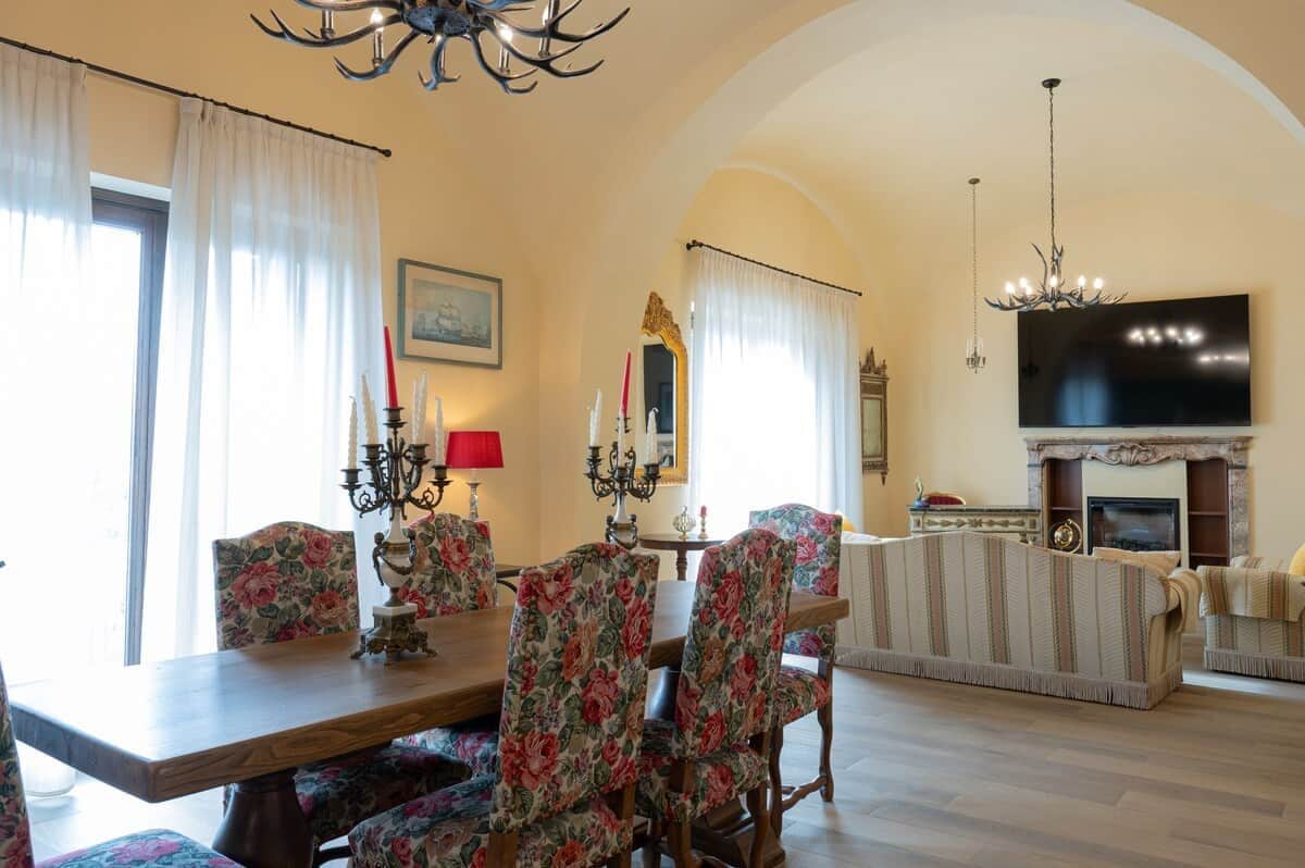 Uma sala de jantar com cadeiras estofadas em floral, uma mesa de jantar de madeira e um lustre.