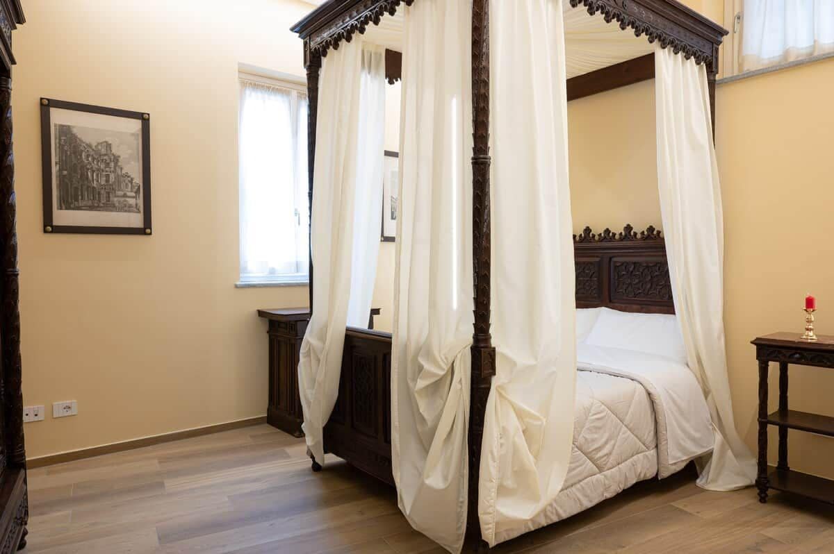 Uma cama com dossel, roupa de cama branca, cabeceira de madeira e cortina.