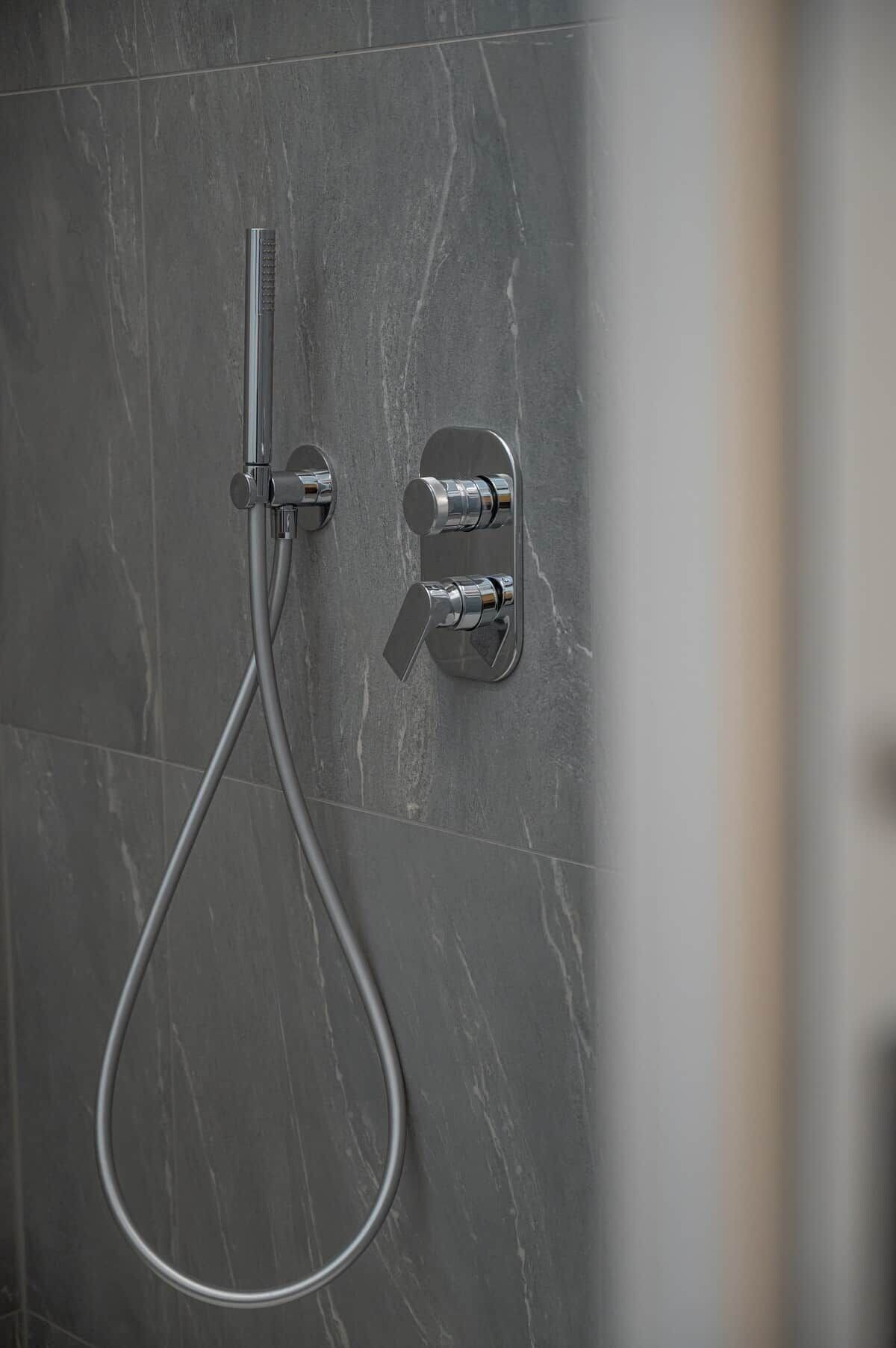 A modern shower with a handheld showerhead and wall-mounted controls.