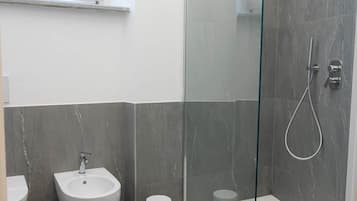 Um banheiro moderno com chuveiro em cabine de vidro, bidê e vaso sanitário.