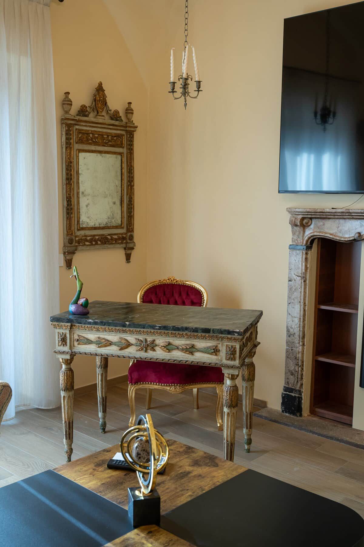 Une pièce avec une table en bois, un fauteuil recouvert de tissu rouge, un lustre et une cheminée.