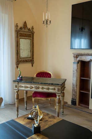Een kamer met een houten tafel, een rode fauteuil, een kroonluchter en een open haard.