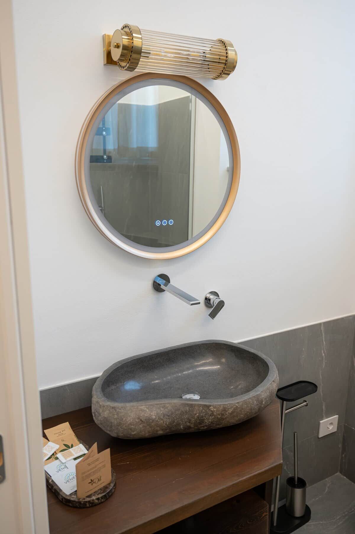 A bathroom with a round mirror, a stone sink, and a towel rack.