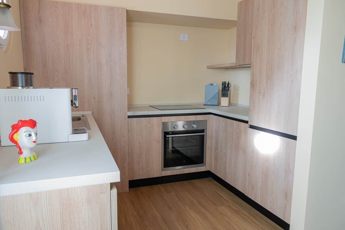 Une cuisine compacte avec des meubles en bois, un four encastré et un plan de travail blanc.