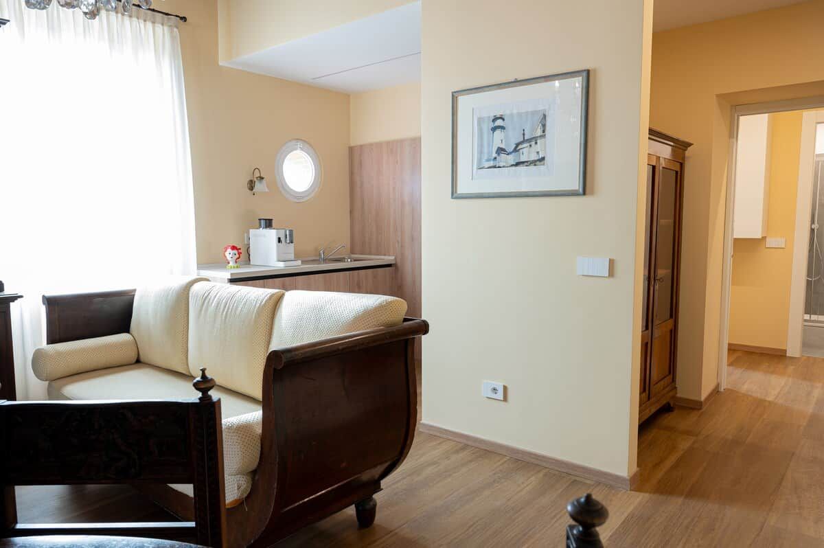 A room with a wooden bed, a round mirror, a small kitchen area, and a framed picture on the wall.