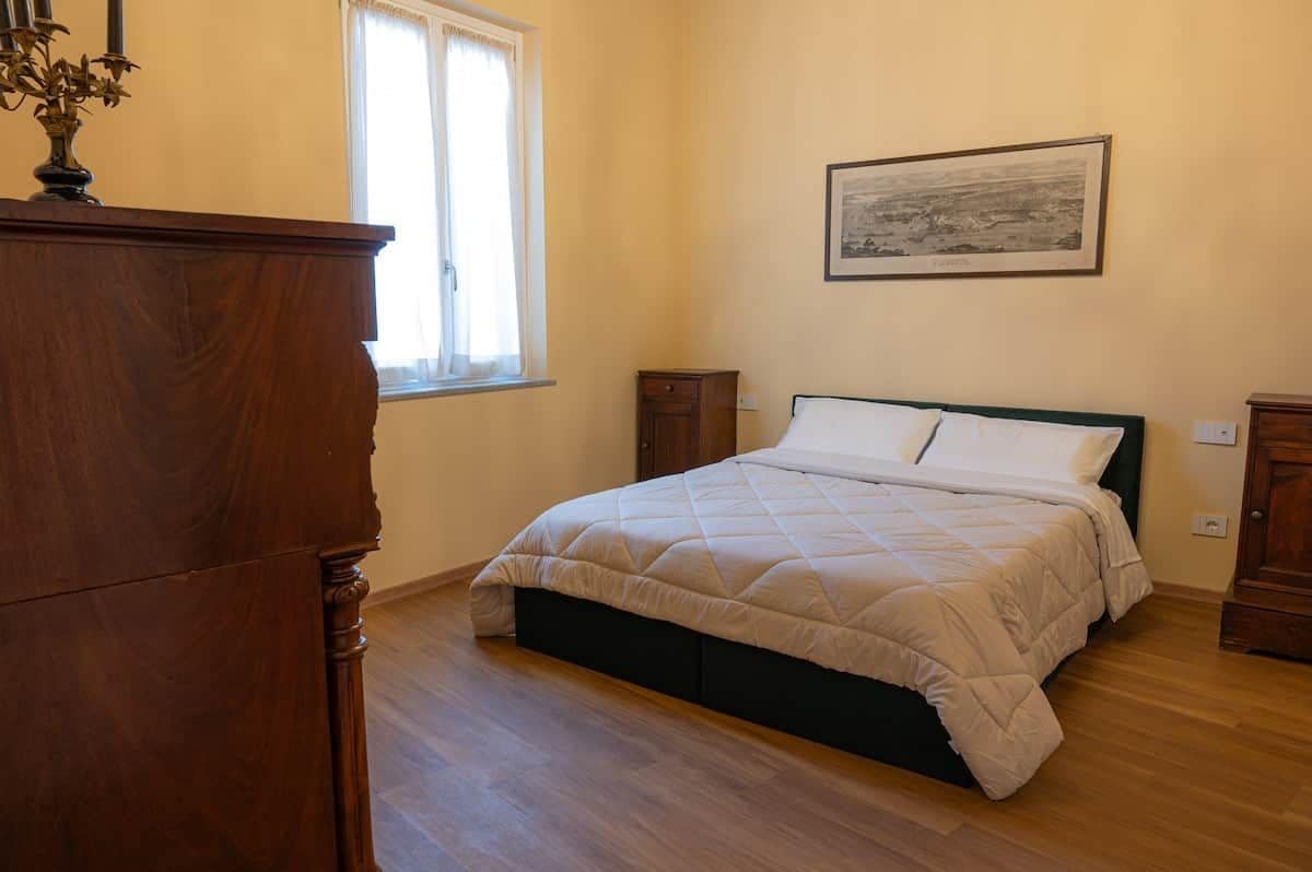 Une chambre à coucher avec un lit, une commode, une fenêtre et un tableau encadré au mur.