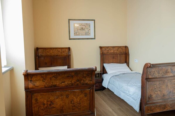 Un dormitorio con dos camas de madera, un cuadro en la pared y una ventana a la izquierda.