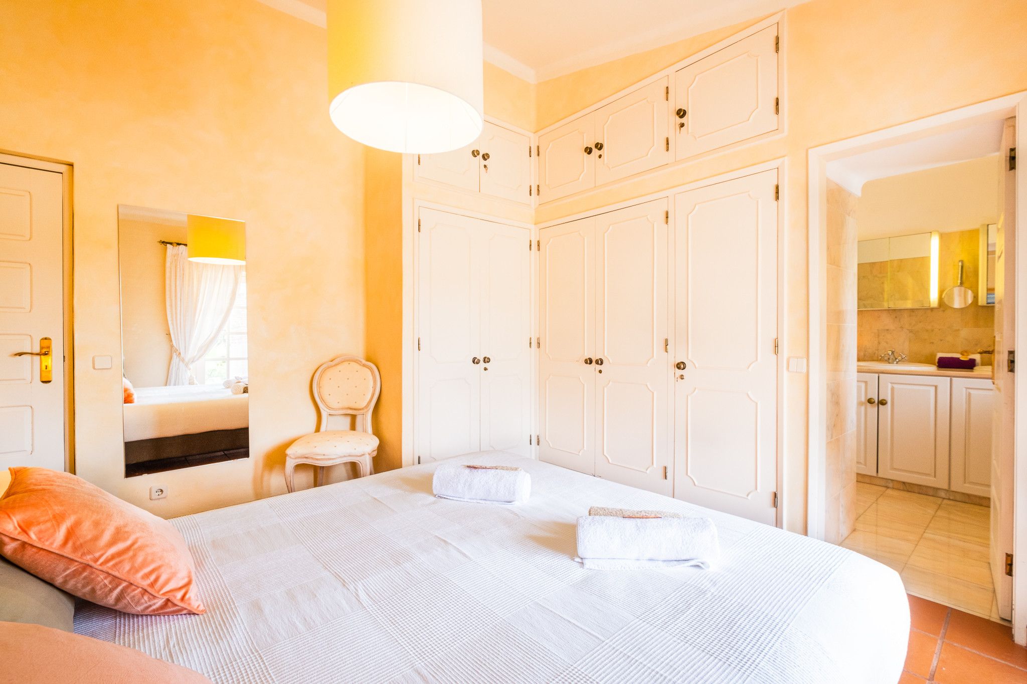 A hotel room with a bed, a chair, a wardrobe, and a bathroom visible through an open door.