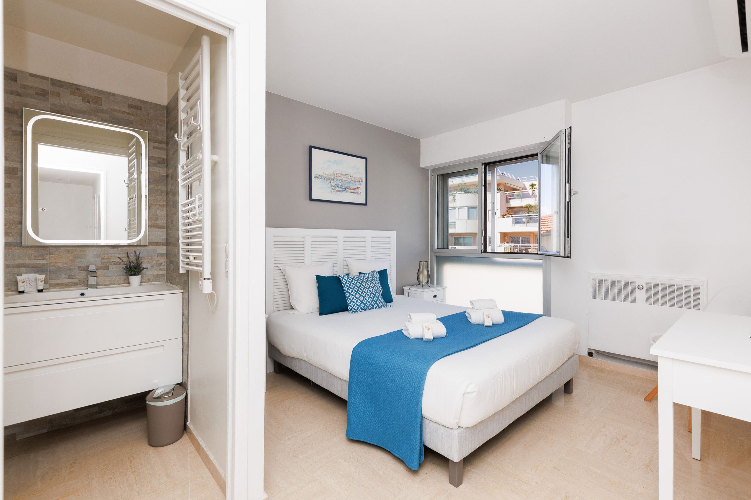 A modern bedroom with a large bed, a bedside table, a window with a view, and a bathroom with a mirror and sink.