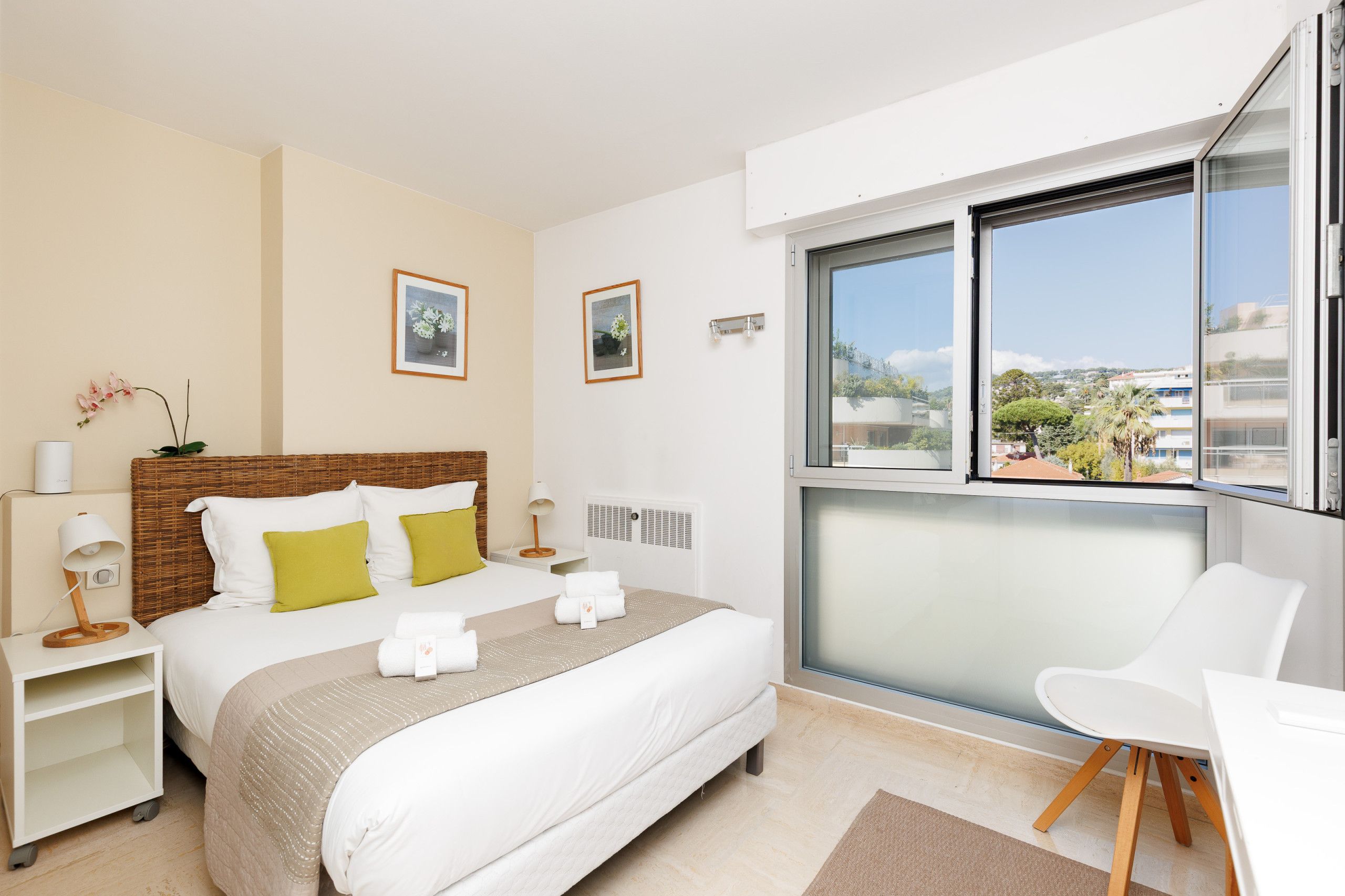 A hotel room with a bed, bedside tables, a chair, a window with a view, and wall-mounted lights.