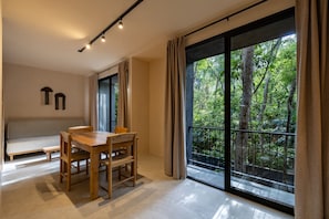 Habitación moderna con una mesa de comedor, sillas, un banco y un amplio ventanal corredero que da a un balcón con vistas a un bosque.