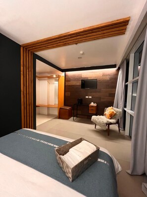 Habitación de hotel moderna con cama, un pequeño rincón de descanso, televisión y puerta corredera que da a un baño.