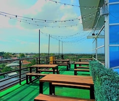 Una terraza al aire libre con mesas y bancos de madera, luces colgantes y vistas a la ciudad.