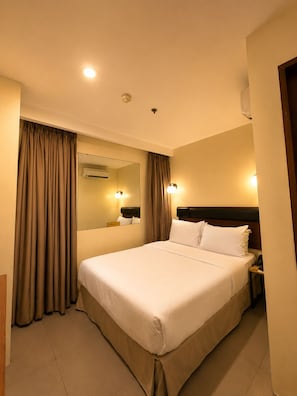Una habitación de hotel con una cama grande, una mesita de noche, un espejo y un equipo de aire acondicionado instalado en la pared.